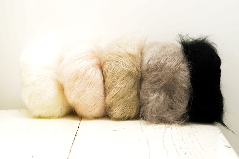 K&ouml;nnte beinhalten: F&uuml;nf Kn&auml;uel Garn in verschiedenen Farbt&ouml;nen von Beige, Braun und Schwarz. Das Garn ist weich und flauschig und perfekt zum Stricken oder H&auml;keln.