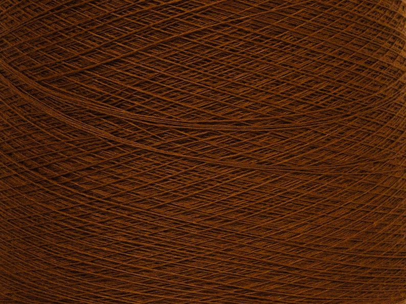 May include: Close-up of a large ball of brown yarn. The yarn is tightly wound, creating a dense, textured surface. The color is a rich, warm brown, with visible strands crisscrossing to form a complex pattern. Ideal for knitting and crochet projects.