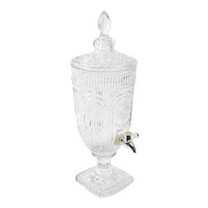 May include: A clear glass beverage dispenser with a decorative, ornate design. The dispenser has a spout with a silver tap and a square base.