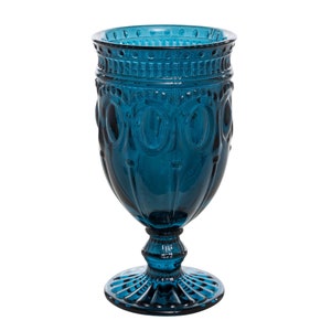 May include: A teal blue glass goblet with a decorative, embossed design. The goblet has a wide base and a tall, slender stem.