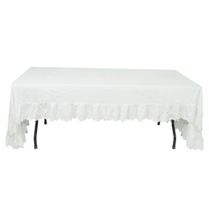 May include: White rectangular tablecloth with a lace trim and a ruffled edge. The tablecloth is draped over a table with black metal legs.