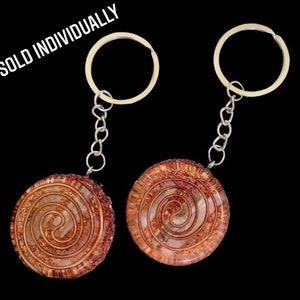 May include: Two silver keyrings with a round, brown and white swirl design. The swirl design is a copper wire embedded in resin. The text "SOLD INDIVIDUALLY" is visible in the image.