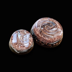 May include: Two clear quartz crystal orbs with copper wire spirals inside. The orbs are embedded in a brown resin base with copper flakes.