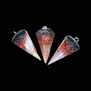May include: Three clear resin pyramid pendants with copper and black glitter embedded inside. The pendants have a silver loop at the top for hanging.