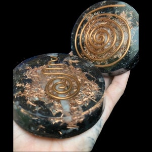 Könnte beinhalten: Zwei schwarze und weiße Kristalluntersetzer mit goldenen Drahtspiralen. Die Untersetzer sind rund und haben eine glänzende Oberfläche.