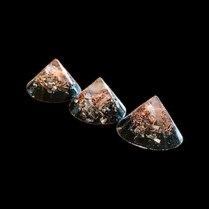 May include: Three clear resin pyramids with copper wire and metallic flakes suspended inside. The pyramids have a dark base and a pointed top, set against a black background. The pyramids are arranged in a diagonal line.