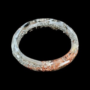 May include: A clear resin ring with silver and copper glitter embedded inside.