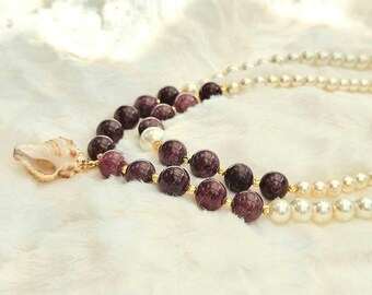 Collar de dos capas de lepidolita y perla de agua dulce con colgante de concha dorada que luce la modelo al aire libre.
