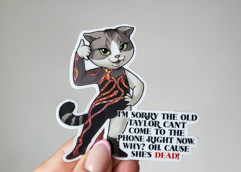 May include: A sticker featuring a cartoon cat with a black and red lava-like outfit, giving a thumbs up. The text reads "I'm sorry the old Taylor can't come to the phone right now. Why? Oh, cause she's dead!"