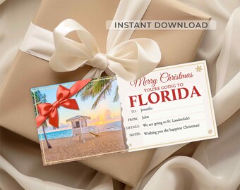 May include: A gift wrapped in brown paper with a cream-colored bow. Attached are two cards: one with a beach scene and a red bow, and another with the text "Merry Christmas, You're Going to Florida."
