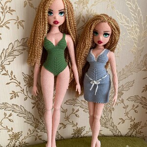 May include: Two crocheted dolls with long blonde hair. The doll on the left is wearing a green swimsuit. The doll on the right is wearing a blue dress. Both dolls have green eyes and red lips.