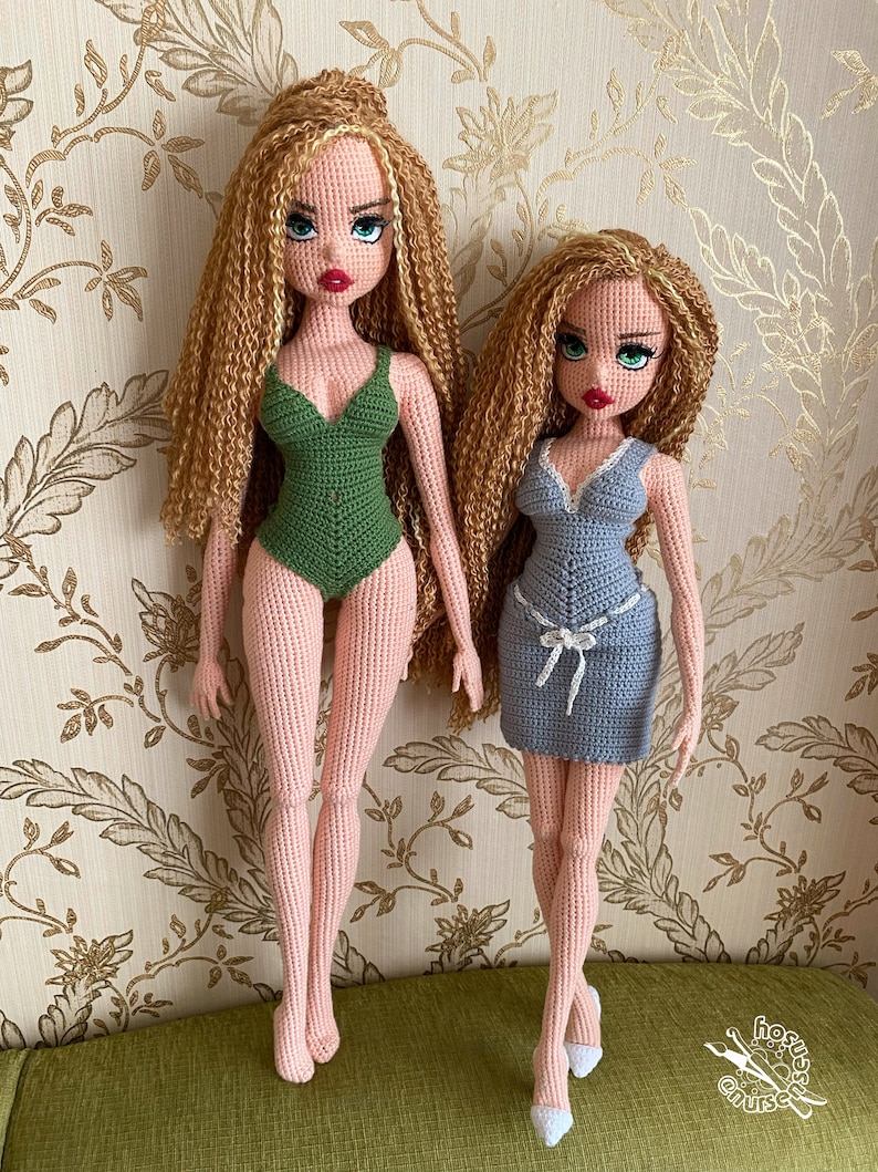 May include: Two crocheted dolls with long blonde hair. The doll on the left is wearing a green swimsuit. The doll on the right is wearing a blue dress. Both dolls have green eyes and red lips.