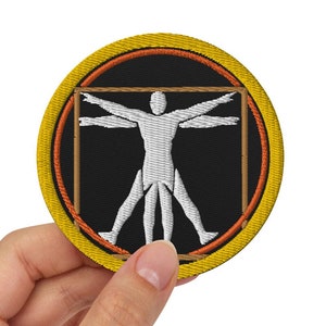 Könnte beinhalten: Ein runder, gelber und orangefarbener gestickter Aufnäher mit einer weißen Silhouette einer Person mit ausgestreckten Armen in einem Quadrat.