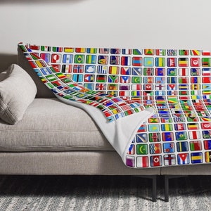 May include: A white couch with a throw blanket featuring a pattern of small, colorful flags from around the world. The blanket is folded over the back of the couch and draped over the front.