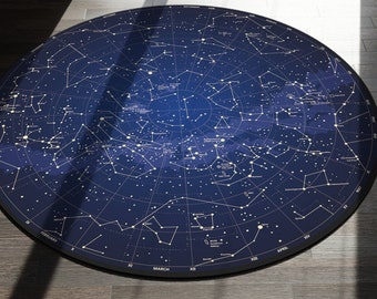 May include: A round, blue rug with a constellation map printed on it. The rug is in a room with a couch and a window.