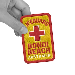 May include: A yellow and red embroidered patch with the text "Lifeguard Bondi Beach Australia" and a red cross.