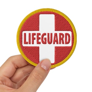 May include: A red and yellow embroidered patch with a white cross and the text "LIFEGUARD" on it.