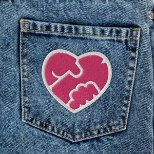 May include: Blue denim jeans with a back pocket featuring a pink heart-shaped patch with a white outline.