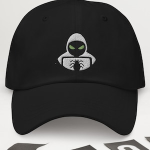 May include: Black baseball cap featuring a white embroidered design of a hooded figure with green eyes holding a spider. The cap has a curved peak and a structured fit. Halloween decorations include paper spiders and bats.