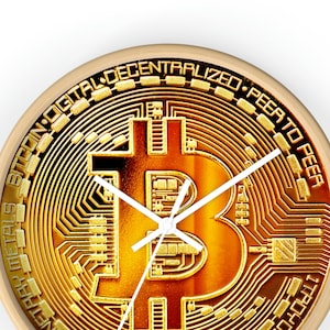 Puede incluir: Un reloj redondo con un diseño de Bitcoin dorado. La esfera del reloj presenta un símbolo de Bitcoin dorado con un patrón de placa de circuito. Las manecillas del reloj son blancas. La esfera del reloj está rodeada por un anillo dorado con el texto "Bitcoin Digital Decentralized Peer to Peer" y "One oz 999 Fine Copper M.B. 1/10th oz Precious Metals 1 Troy oz 2022".