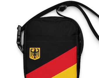 Könnte beinhalten: Schwarze Umhängetasche mit diagonalem Streifenmuster in Rot, Gelb und Schwarz. Die Tasche zeigt die Farben der deutschen Flagge und das deutsche Wappen.