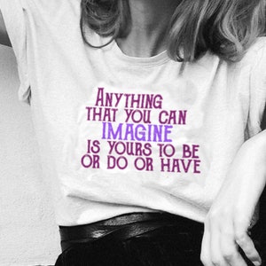 Könnte beinhalten: Ein weißes T-Shirt mit einer lila und pinkfarbenen Grafik, auf der "Anything that you can imagine is yours to be or do or have." steht.