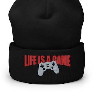 Può includere: Berretto nero con un designo ricamato rosso che dice "Life is a game" e un controller per videogiochi grigio.