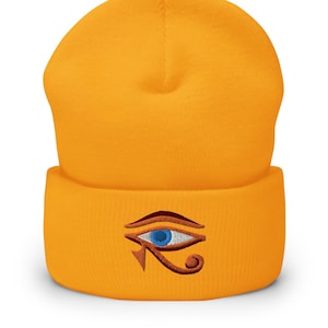 Puede incluir: Un gorro amarillo con un diseño bordado de ojo de Horus en marrón y azul.