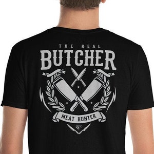 Könnte beinhalten: Schwarzes T-Shirt mit einem weißen Grafikdesign aus gekreuzten Metzgermessern und einem Banner mit der Aufschrift "The Real Butcher Meat Hunter".