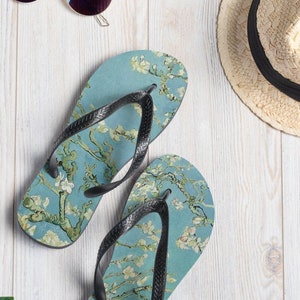 Könnte beinhalten: Ein Paar blaue Flip-Flops mit einem Blumenmuster. Der Druck zeigt ein Gemälde eines blühenden Mandelbaums vor blauem Himmel.