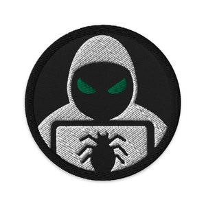 Peut inclure: Écusson brodé circulaire noir avec un contour blanc représentant une figure encapuchonnée aux yeux verts et un motif d'araignée. Le design est contrasté et détaillé.