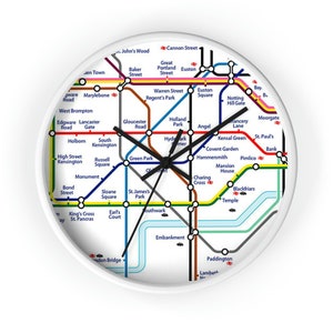 May include: A white circular clock with a black clock face featuring a map of the London Underground. The clock face shows the names of various London Underground stations, including Baker Street, Euston, and Charing Cross. The clock hands are black.