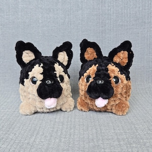 May include: Two plush dog toys made of soft yarn. The left toy features black and beige fur with large dark eyes and a small pink tongue. The right toy features black and brown fur with large dark eyes and a small pink tongue. Both are stuffed.