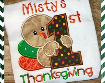 May include: A white onesie with a brown turkey holding a brown and orange number one with colorful polka dots. The onesie says "Misty's 1st Thanksgiving" in orange and green embroidery.