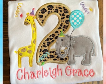 May include: A white t-shirt with a leopard print number two, a giraffe and an elephant. The shirt has the name "Charleigh Grace" embroidered on the bottom.