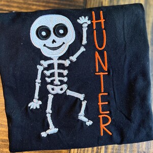 May include: Black t-shirt with a white skeleton design and the name "HUNTER" in orange lettering.