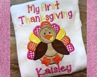 May include: White onesie with the text "My First Thanksgiving" and a colorful embroidered turkey with the name "Kaisley" underneath.