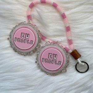 May include: Pink and white beaded earrings with a pink circle pendant that says "EW PEOPLE" in black lettering. The earrings are attached to a pink and white beaded lanyard with a brown leather key chain.