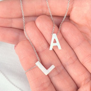 Puede incluir: Dos collares de plata con colgantes de letras de ópalo blanco. Los collares están superpuestos y presentan las letras 'A' y 'L'.