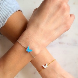May include: Two delicate butterfly charm bracelets. One bracelet features a blue opal butterfly charm, while the other features a white opal butterfly charm.