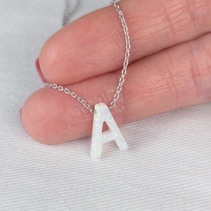 Puede incluir: Un collar de cadena de plata con un colgante de letra A de ópalo blanco.