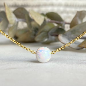 May include: A delicate gold chain necklace with a single white opal gemstone pendant.