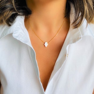 May include: A gold chain necklace with a white hamsa hand pendant.
