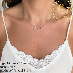 May include: A silver necklace with two interlocking circles, one 10 mm and the other 15 mm in diameter. The necklace is 16 inches long and is shown on a model who is 5'4" tall. Rings: 10 mm & 15 mm Finish: Silver Length: 16" (model 5' 4")