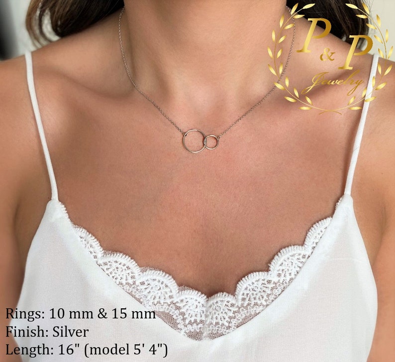 May include: A silver necklace with two interlocking circles, one 10 mm and the other 15 mm in diameter. The necklace is 16 inches long and is shown on a model who is 5'4" tall. Rings: 10 mm & 15 mm Finish: Silver Length: 16" (model 5' 4")
