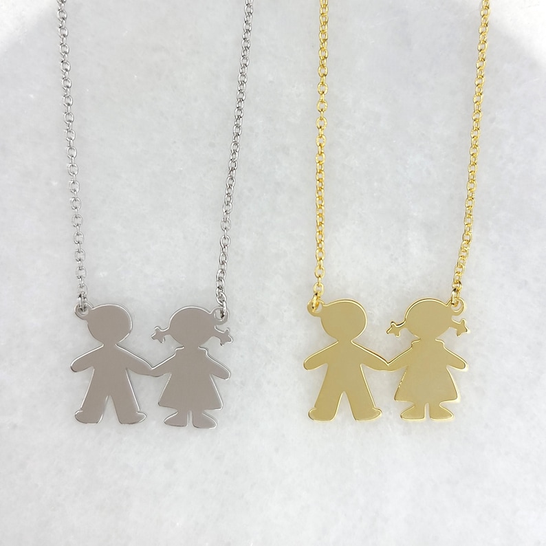 May include: Two silver and gold necklaces with a pendant of two figures holding hands. The figures are a boy and a girl.