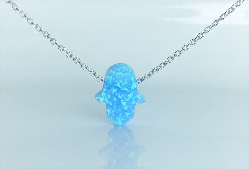 May include: A silver chain necklace with a light blue opal hamsa hand pendant.