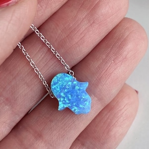 May include: A silver chain necklace with a blue opal hamsa hand charm. The hamsa hand is a symbol of protection and good luck.