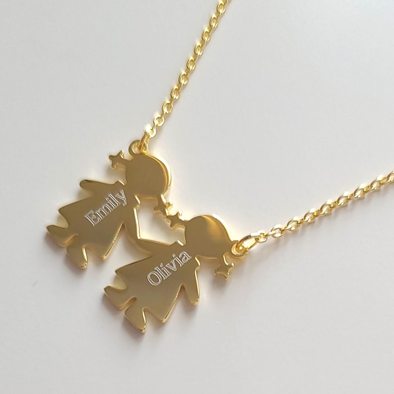 May include: Gold necklace with two figures holding hands. The figures are engraved with the names "Emily" and "Olivia".