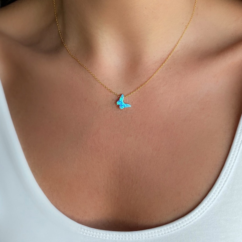 May include: A delicate gold chain necklace with a small blue opal butterfly pendant.